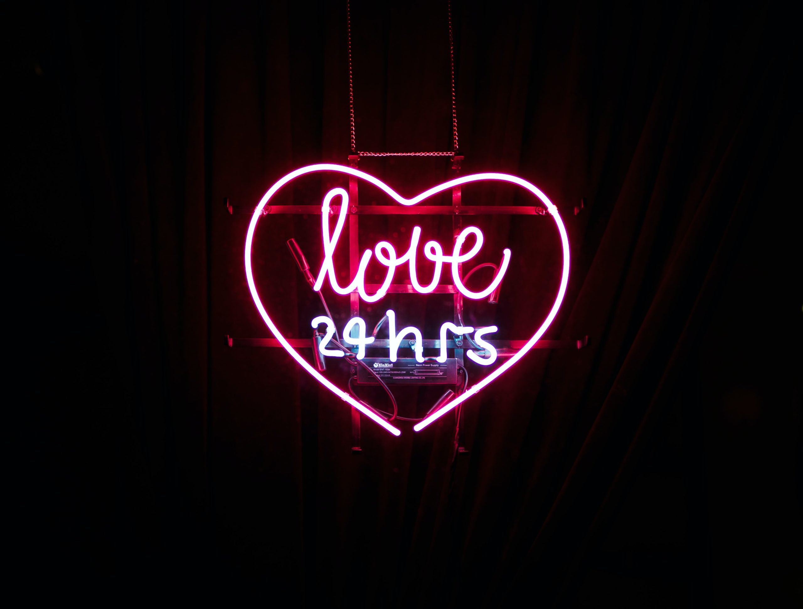neon sign in the shape of a heart reading "love 24 hrs"
